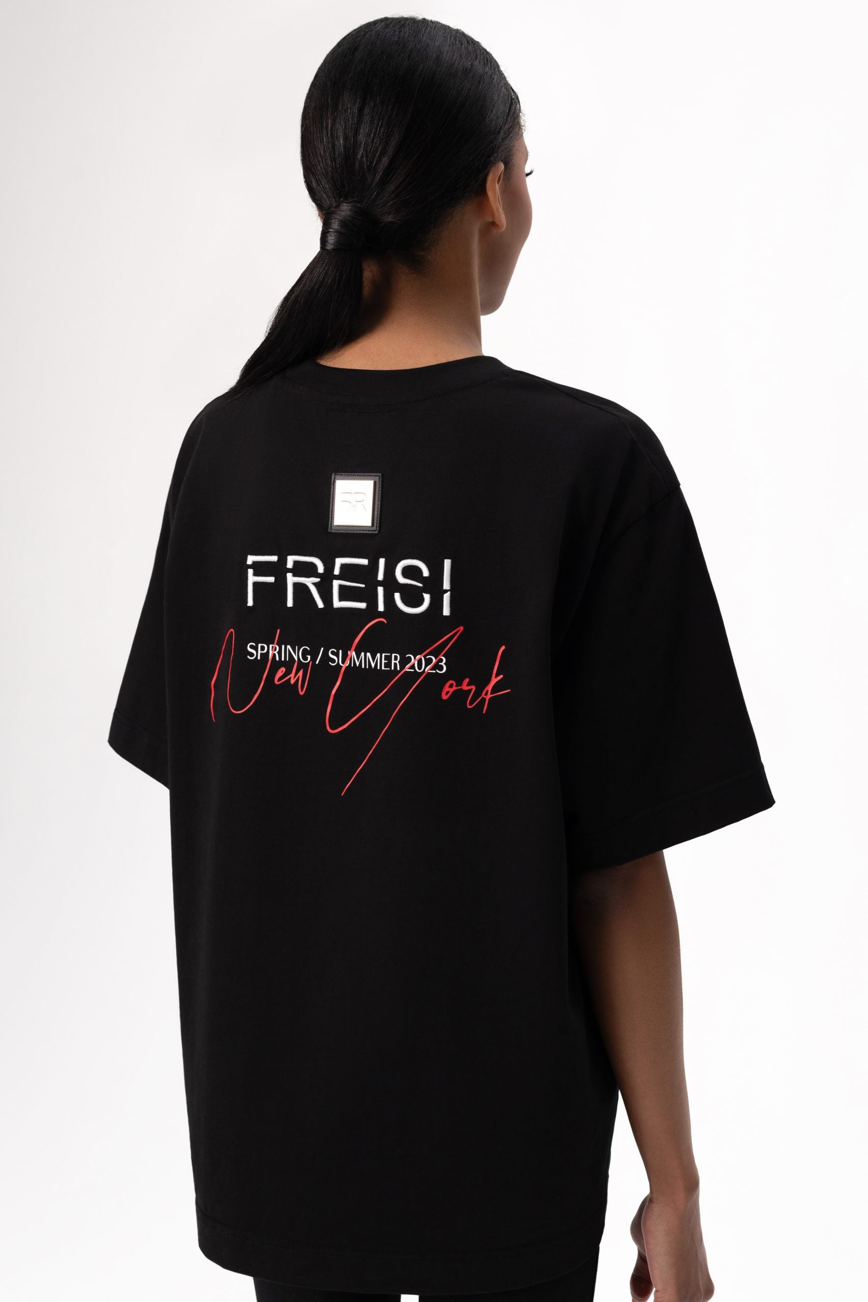 A branded gold metal and leather label on the reverse, close to the embroidered FREISI logo, marks this T-shirt as a symbol of authentic craftsmanship and sophistication